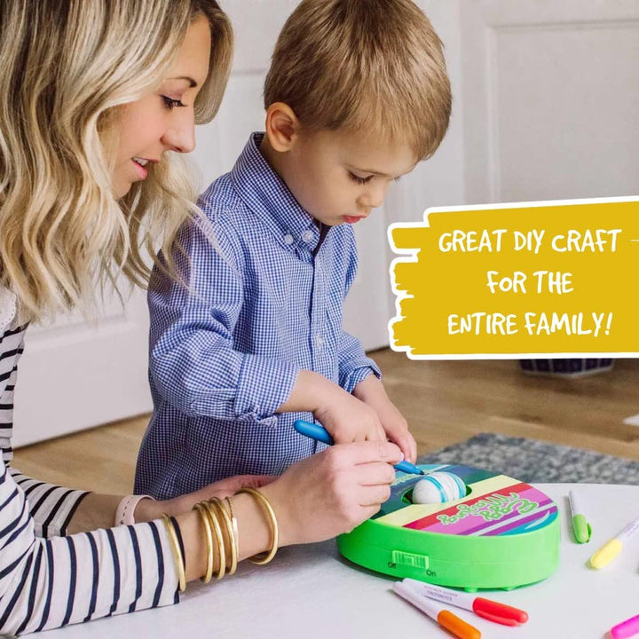 An adult and child decorate an egg together using the green rotating egg decorator