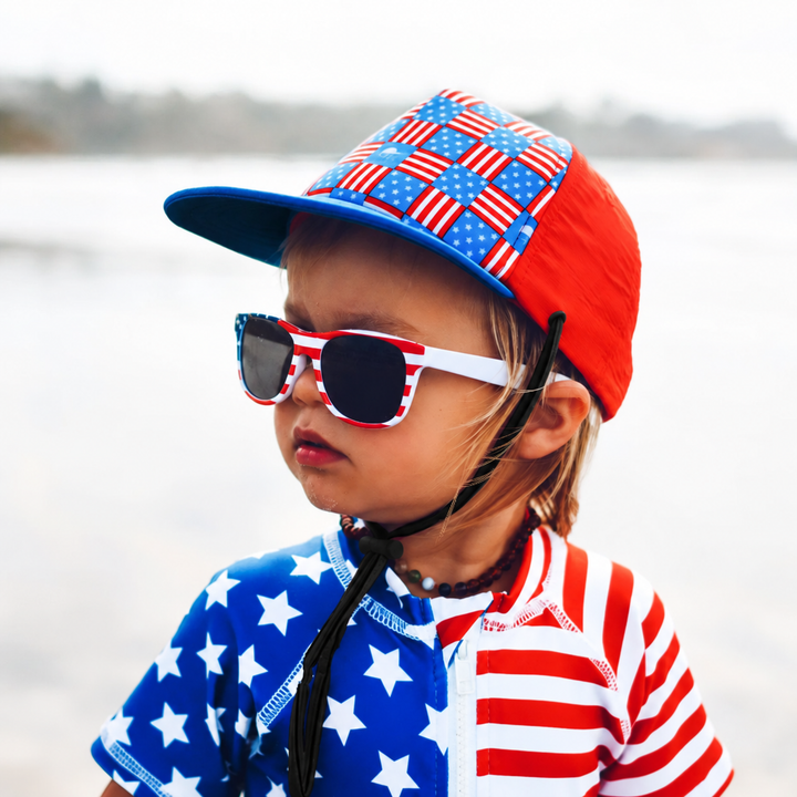 Child wearing a red and blue American flag-print cap with sunglasses