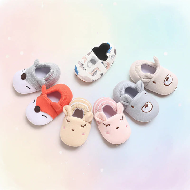 Animal-face and dinosaur-print baby shoes arranged in a circle on a pastel background.
