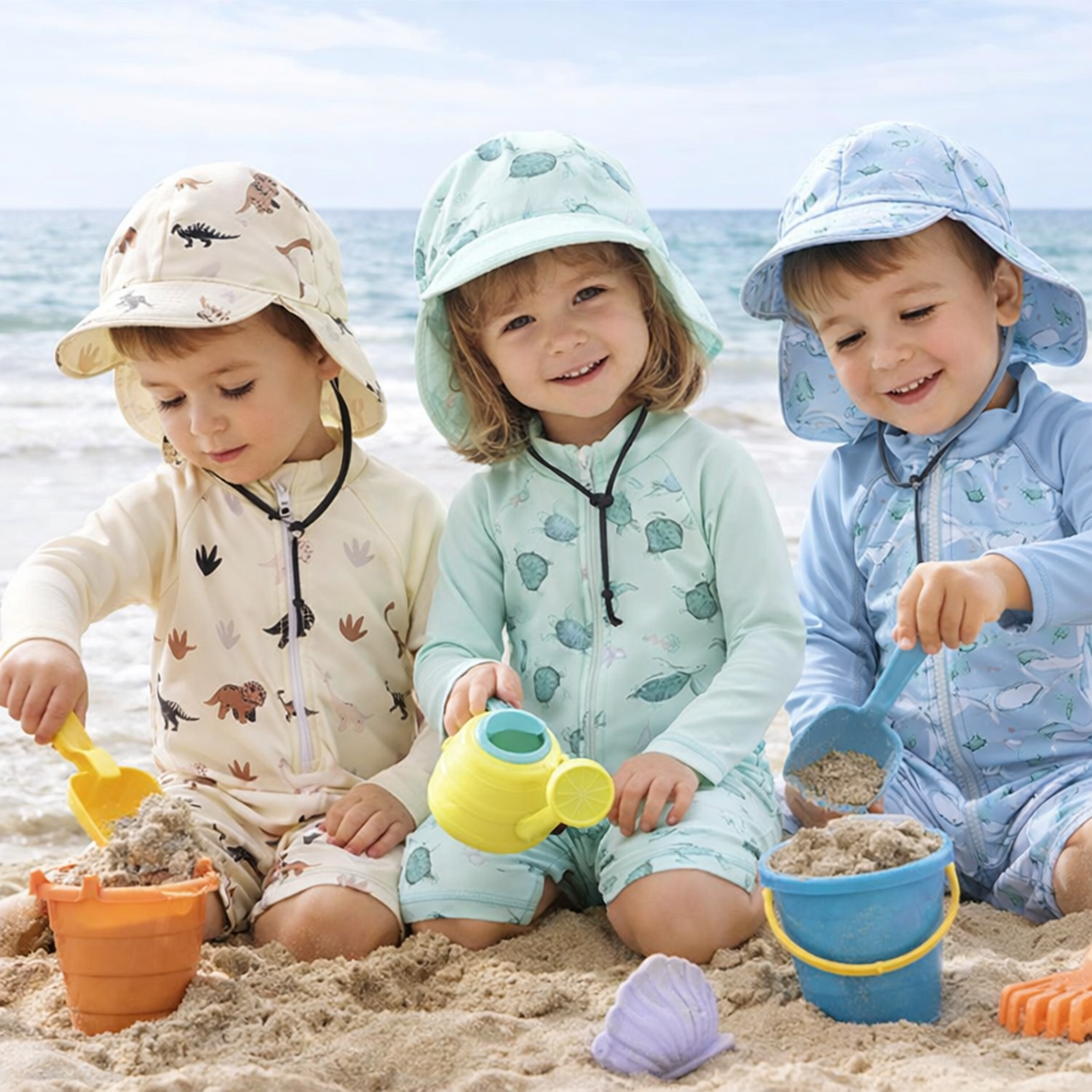 Three children playing in the sand in dinosaur, turtle, and whale swim sets with matching hats.