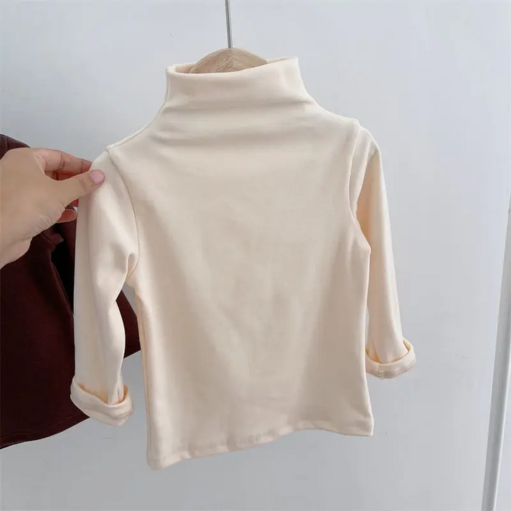 Apricot baby sweater on a hanger, showing its high neckline and long sleeves.