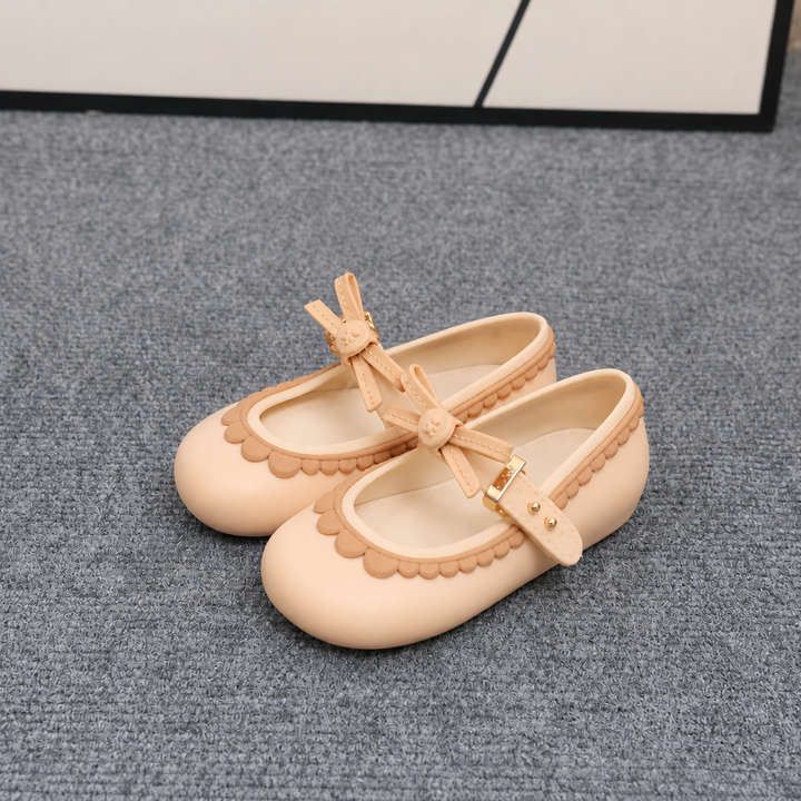Apricot Mary Jane shoes showing bow straps and scalloped edging on gray carpet