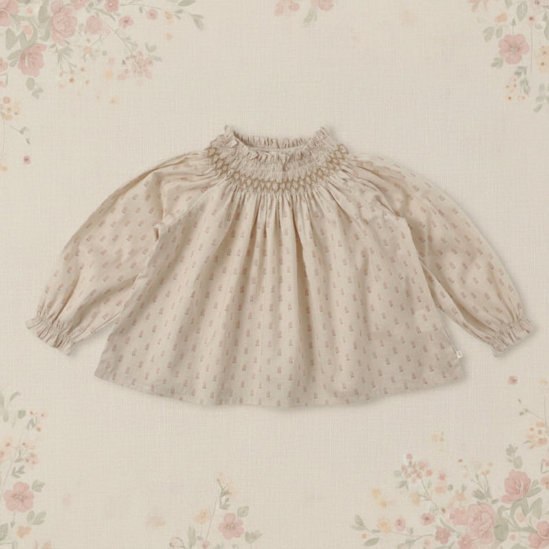 Apricot top with a small pink print, gathered neckline, and puffed sleeves on a floral background
