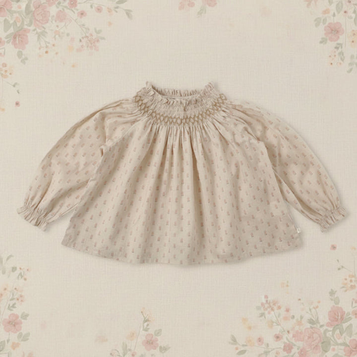 Apricot top with a small pink print, gathered neckline, and puffed sleeves on a floral background