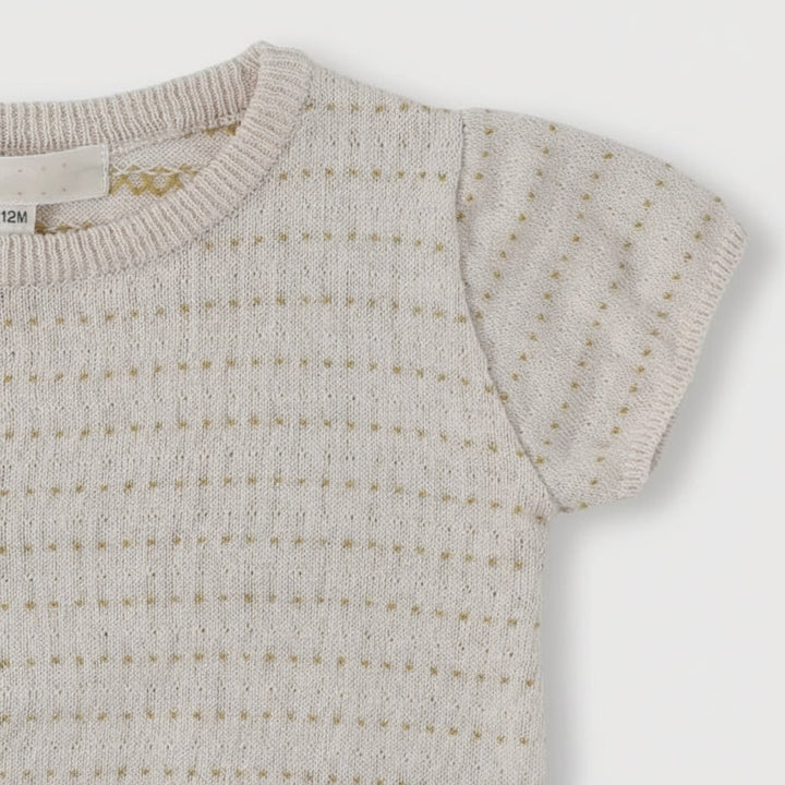Close-up of an Apricot knit top with a round neckline, short sleeve, and pointelle pattern