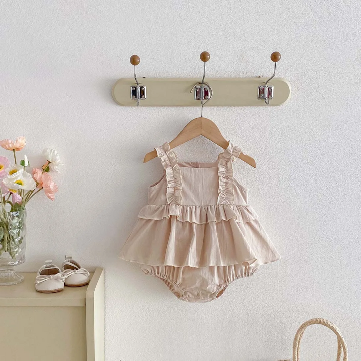 Apricot baby dress romper with ruffled straps hanging from a wall hook