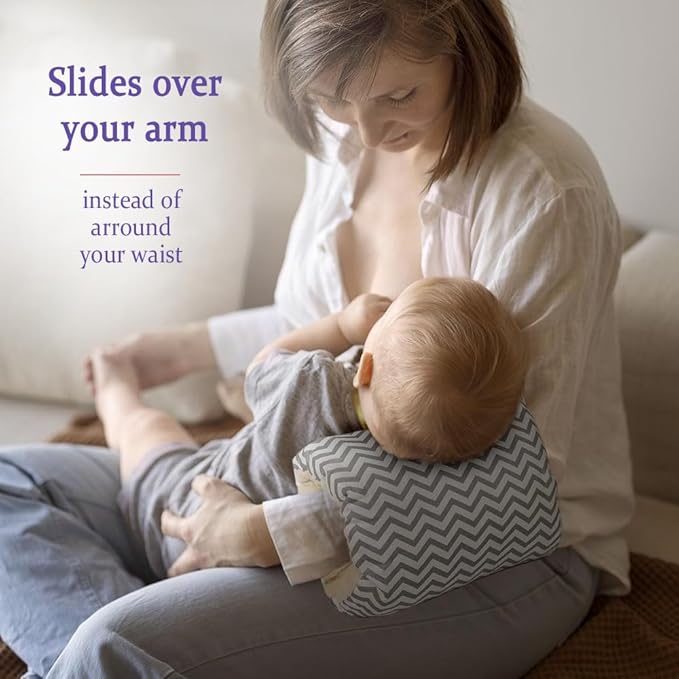 Parent feeding a baby with a gray chevron nursing pillow fitted over the arm.