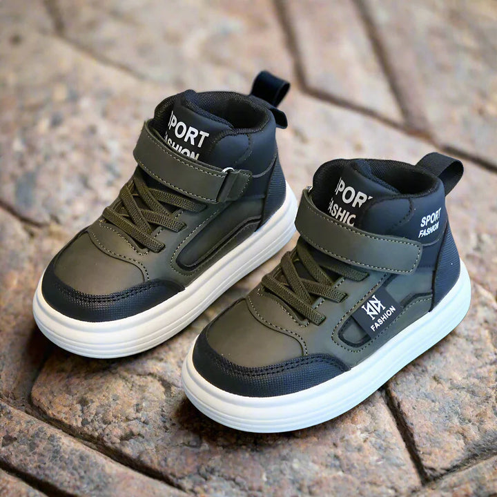 Pair of army green high-top sneakers with black panels and white soles on cobblestones