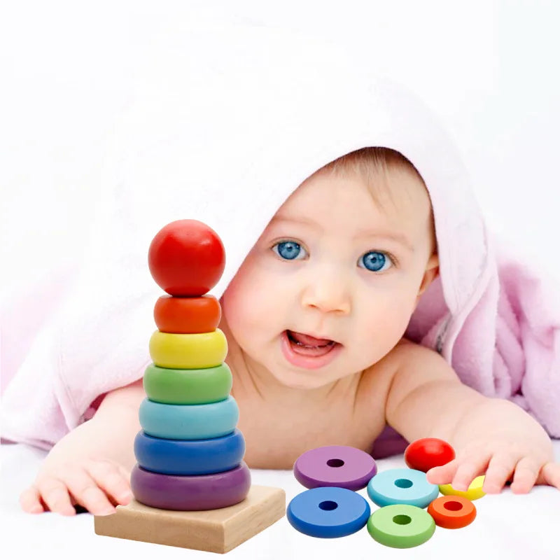 Baby beside a bright wooden stacking tower with loose colored rings on a white surface