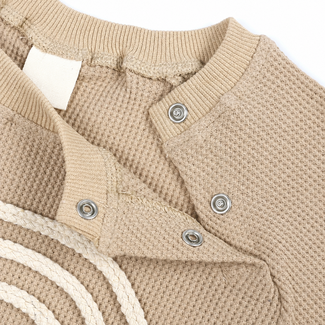 Open shoulder snap fastening on a beige textured baby bodysuit