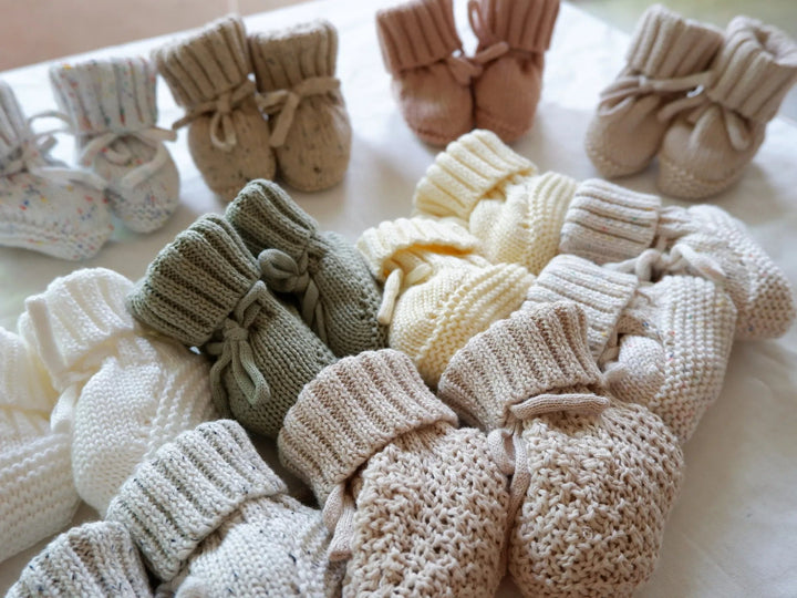 Close-up of knitted baby booties in green, yellow, pink, and neutral shades.