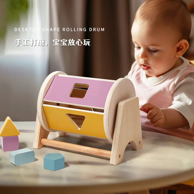 Baby exploring a wooden shape-sorting drum with colorful panels and geometric blocks