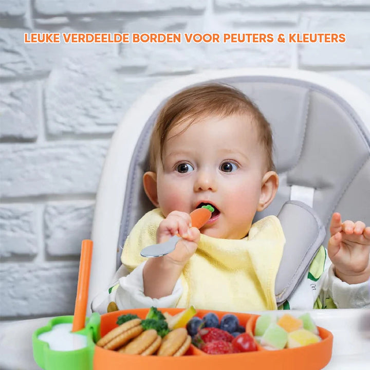 Baby using a carrot-handled utensil beside a divided plate on a high chair tray
