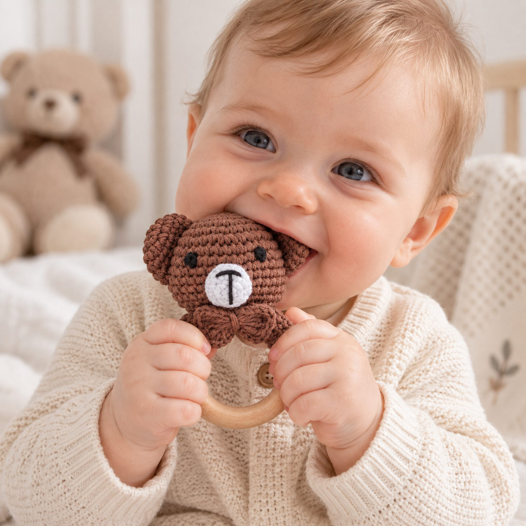 Baby holding a brown crocheted bear rattle with a wooden ring