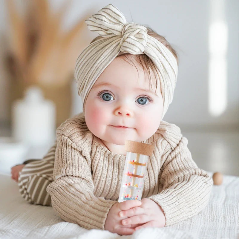 Baby in a knit sweater holding a rainstick rattle with wooden ends