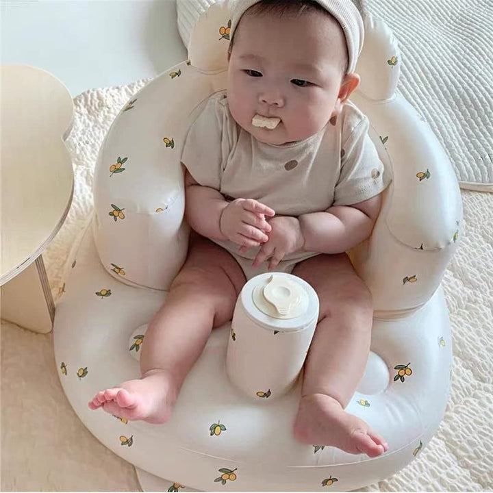 Baby sitting in a white inflatable seat with small yellow and green prints, viewed from above.