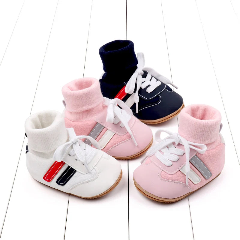Pink, white, and navy baby shoes with knit ankle cuffs and white laces on a white plank background