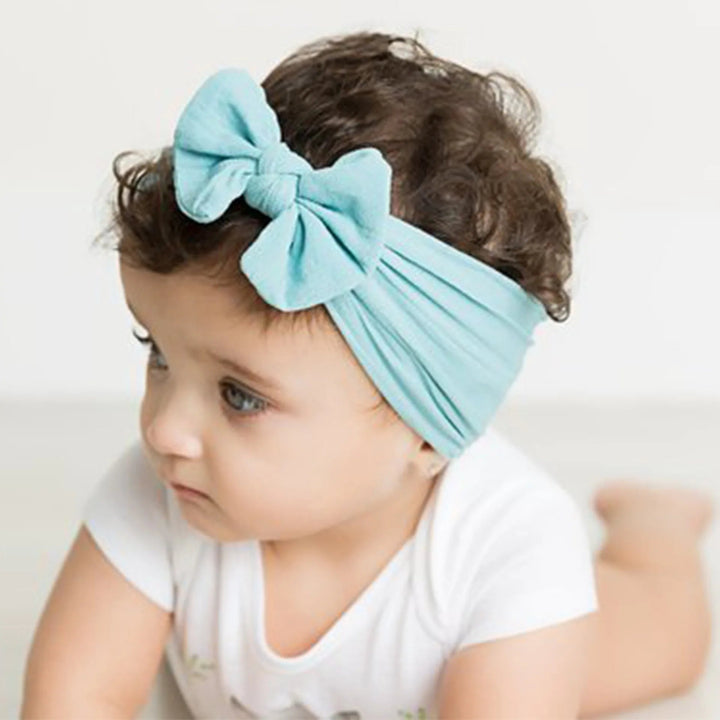 Baby wearing a light blue bow headband with a white outfit