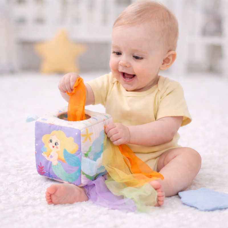 Baby pulling an orange fabric scarf from a mermaid sensory cube
