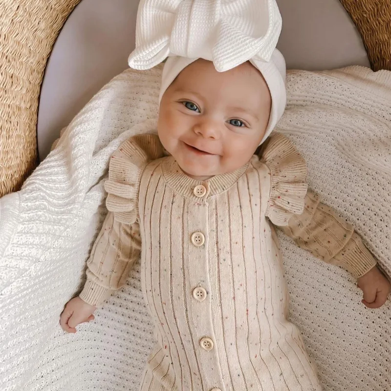 Smiling baby wearing a beige button-front knit romper and white bow headband