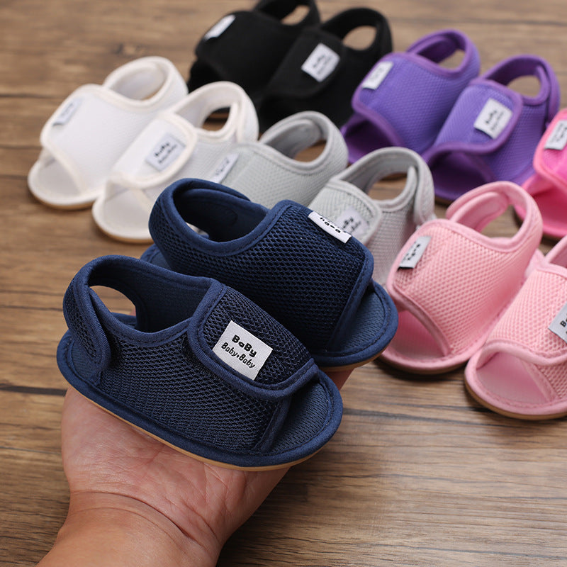 Hand holding navy baby sandals in front of a lineup of other sandal colors