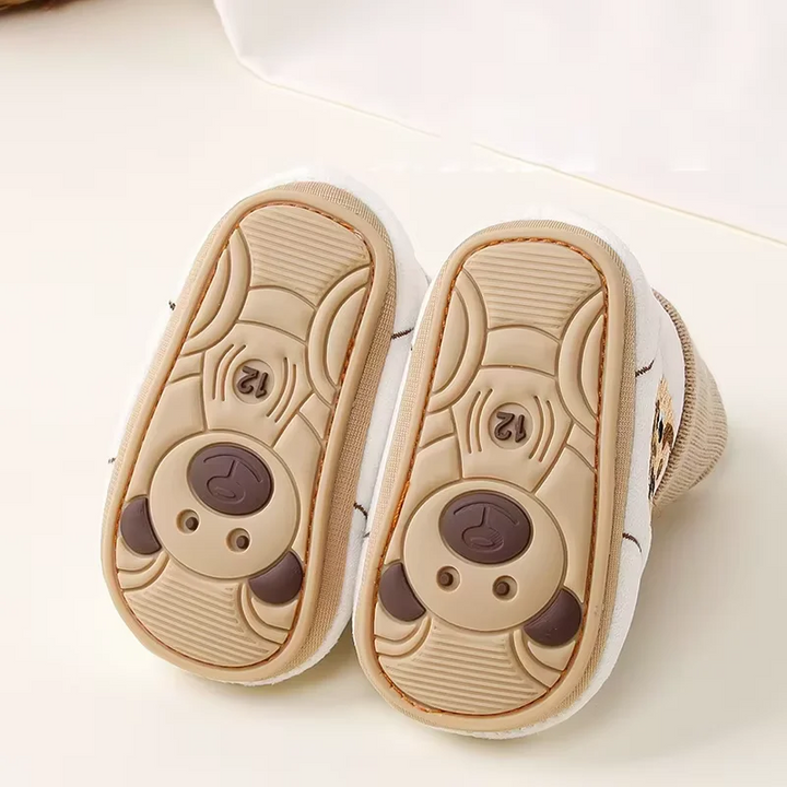 Bottom view of baby shoes showing tan soles with textured grip patterns and animal-face details.