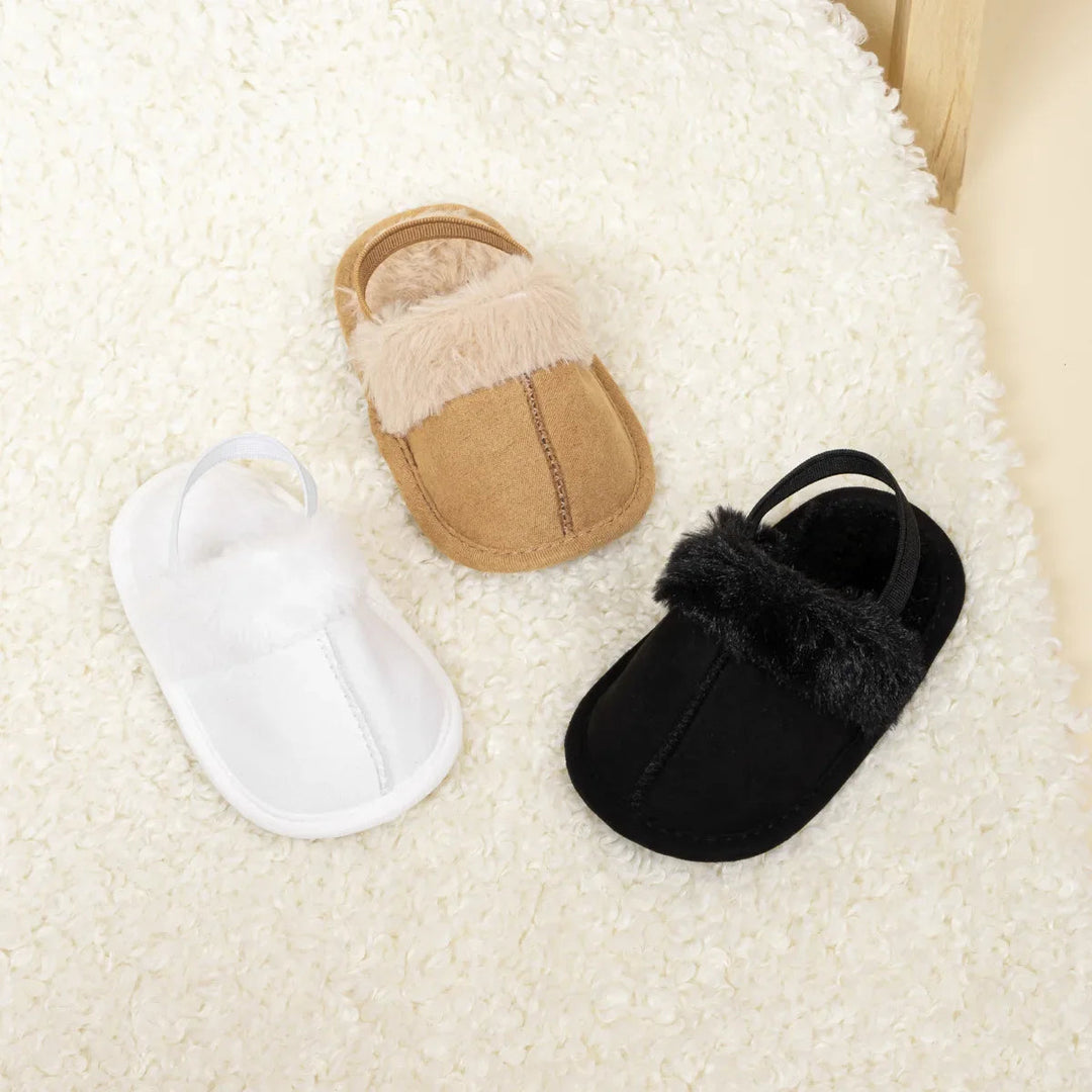 White, tan and black baby slippers with plush trim and heel straps, viewed from above