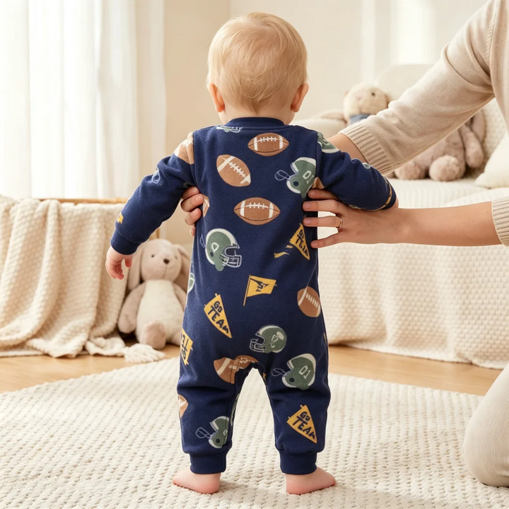 Rear view of a baby wearing a navy football-print fleece jumpsuit while supported by an adult