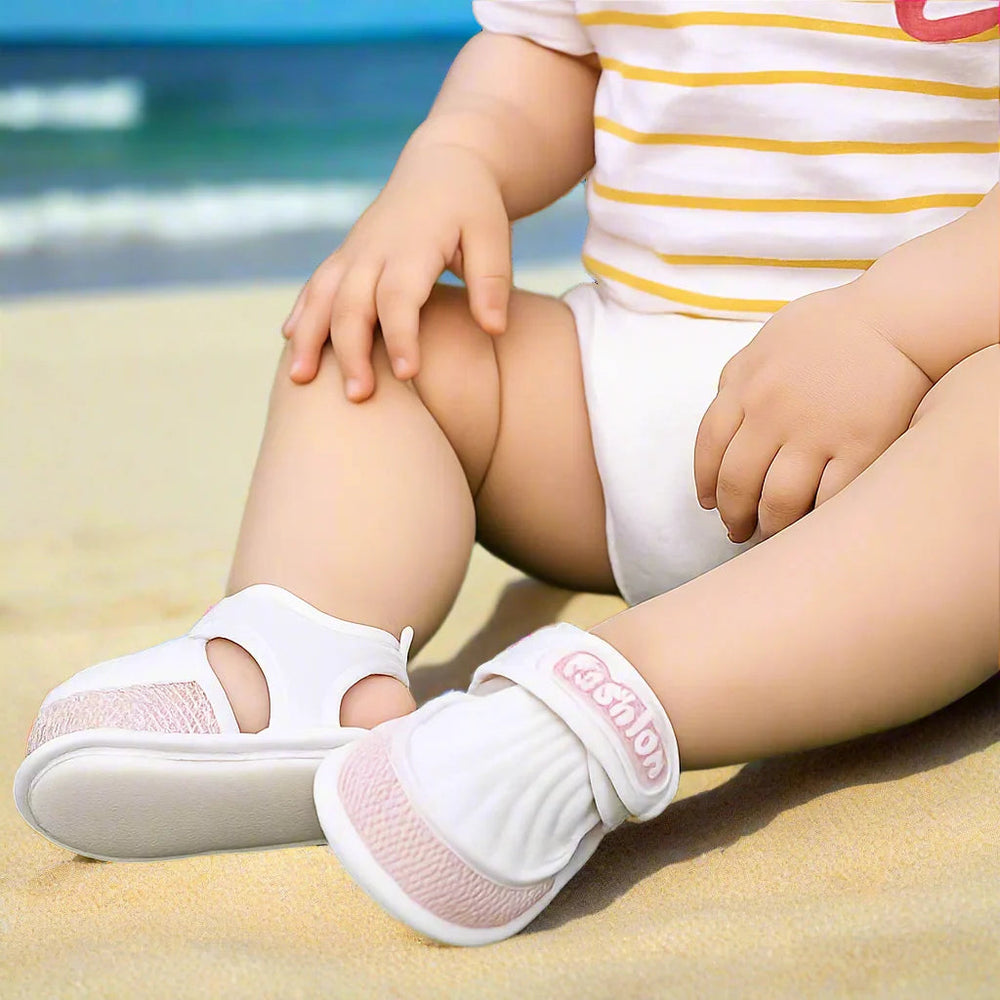 Seated baby wearing white sandals with pink trim and adjustable straps