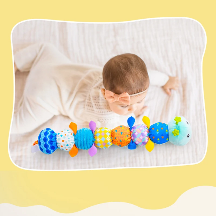Baby sitting behind a blue caterpillar rattle with colorful fabric segments