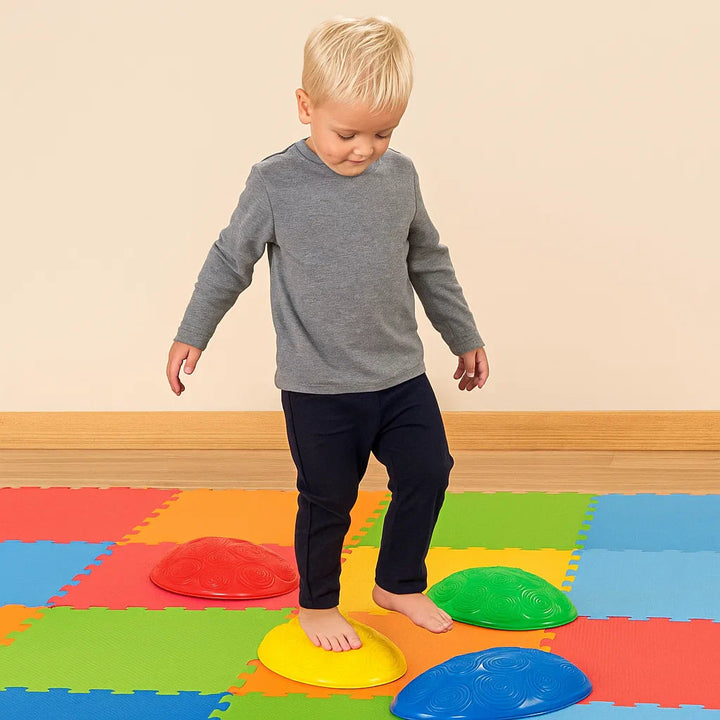 Barefoot child practicing balance with colorful stepping stones on a foam play mat