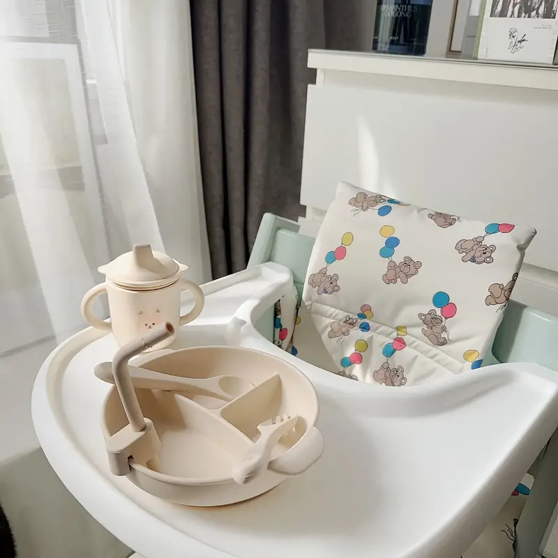 Balloon-bear high chair cushion shown behind a white tray with a plate and cup