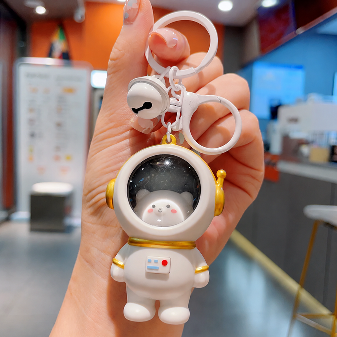 Bear astronaut keychain with a white spacesuit, gold-tone helmet trim, and bell