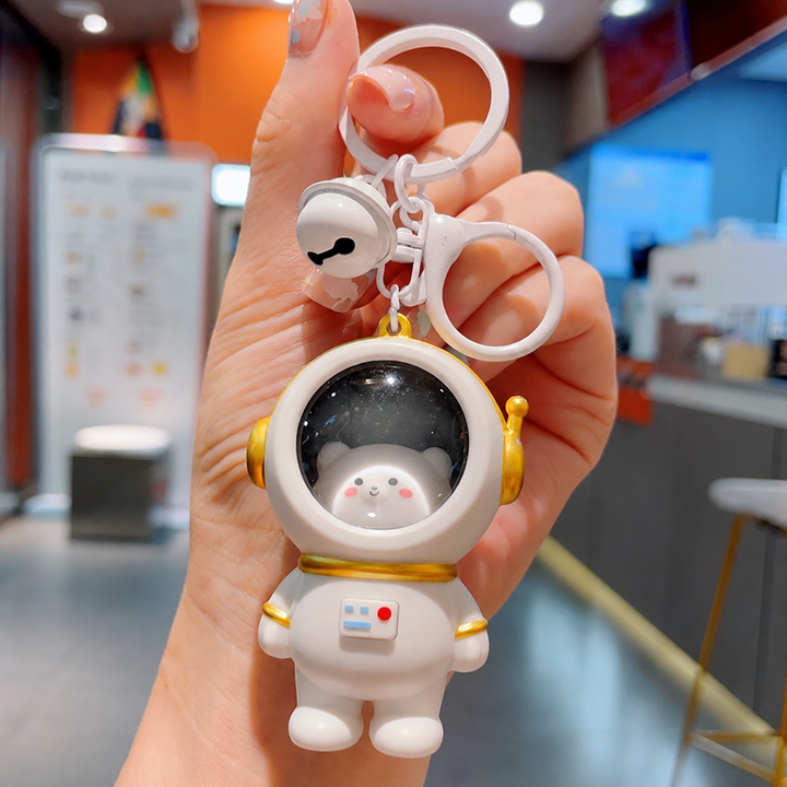 Bear astronaut keychain with a white spacesuit, gold-tone helmet trim, and bell