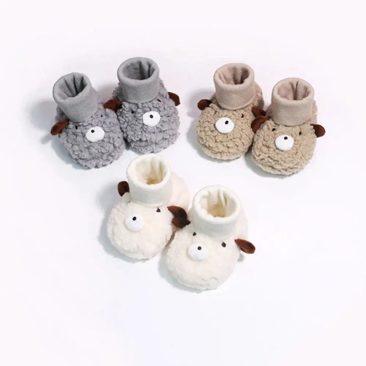 Three pairs of bear-face baby slippers in gray, cream, and khaki with ribbed ankle cuffs