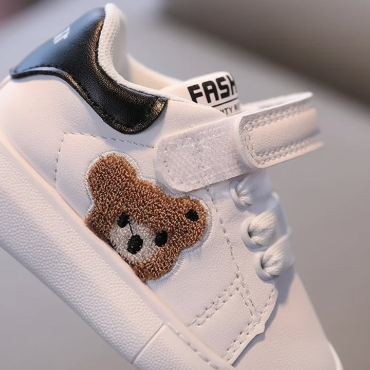 Close-up of an open hook-and-loop strap beside raised bear embroidery and a black heel panel.