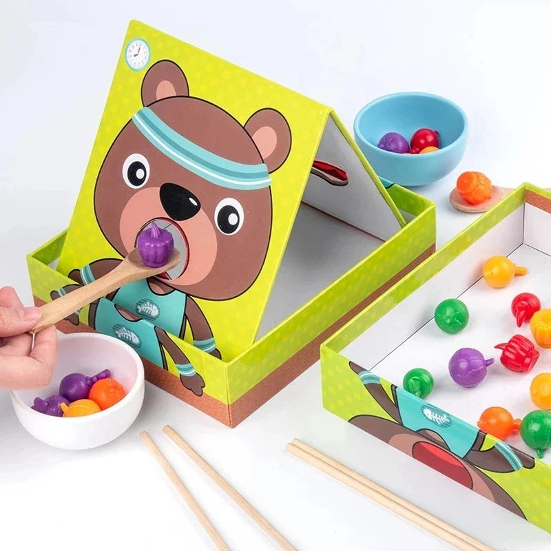 Bear feeding board with colorful food pieces, two bowls, a spoon, and chopsticks