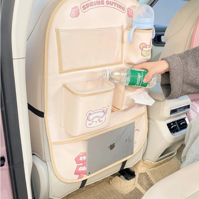 Hand holding a bottle beside a beige bear organizer with a tablet in the lower pocket