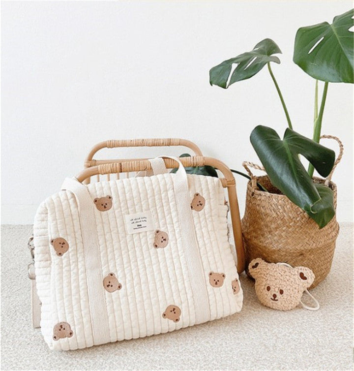 Bear-print quilted diaper bag with long handles beside a wooden chair