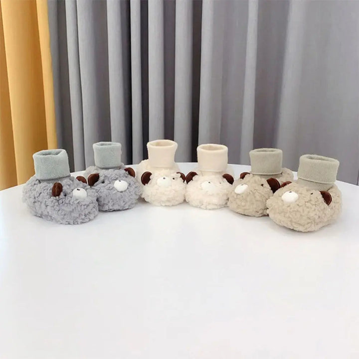 Three pairs of neutral-colored bear baby slippers lined up with their ribbed cuffs upright