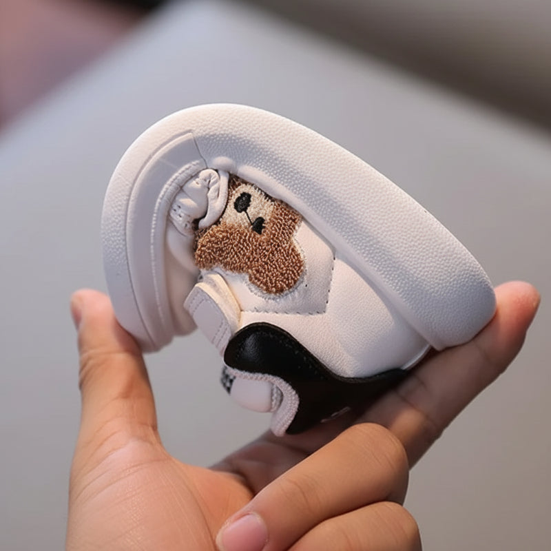 A hand bends a white bear sneaker to show the flexible sole and black heel panel.