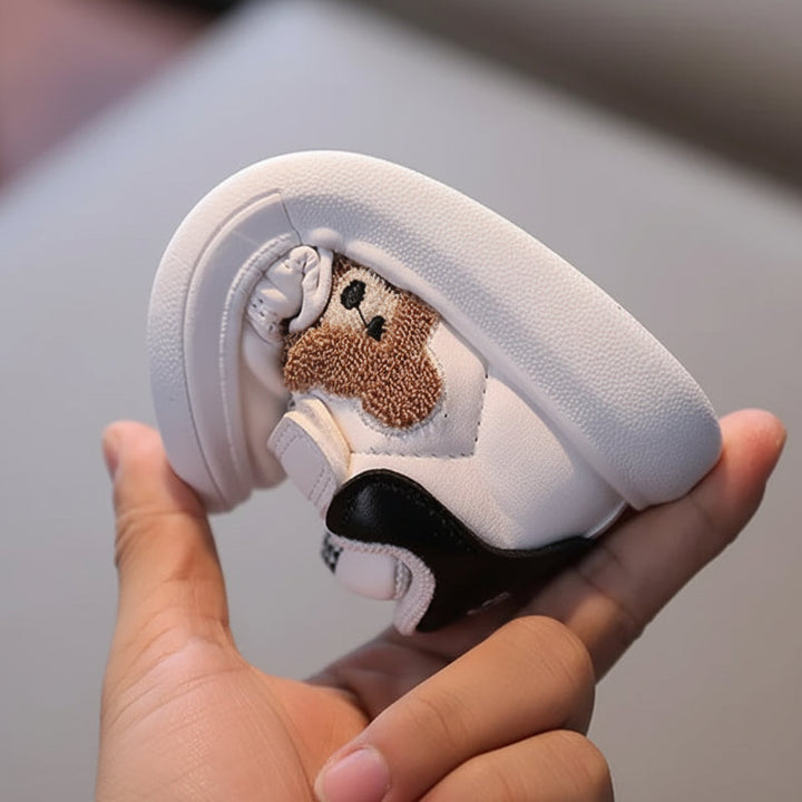 A hand bends a white bear sneaker to show the flexible sole and black heel panel.