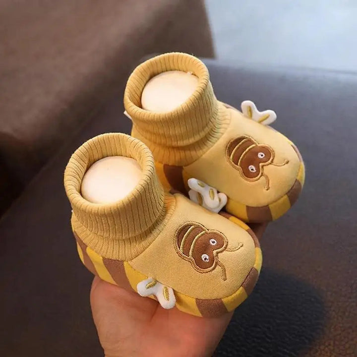 Yellow bee indoor shoes held in one hand, showing striped edges and side wings