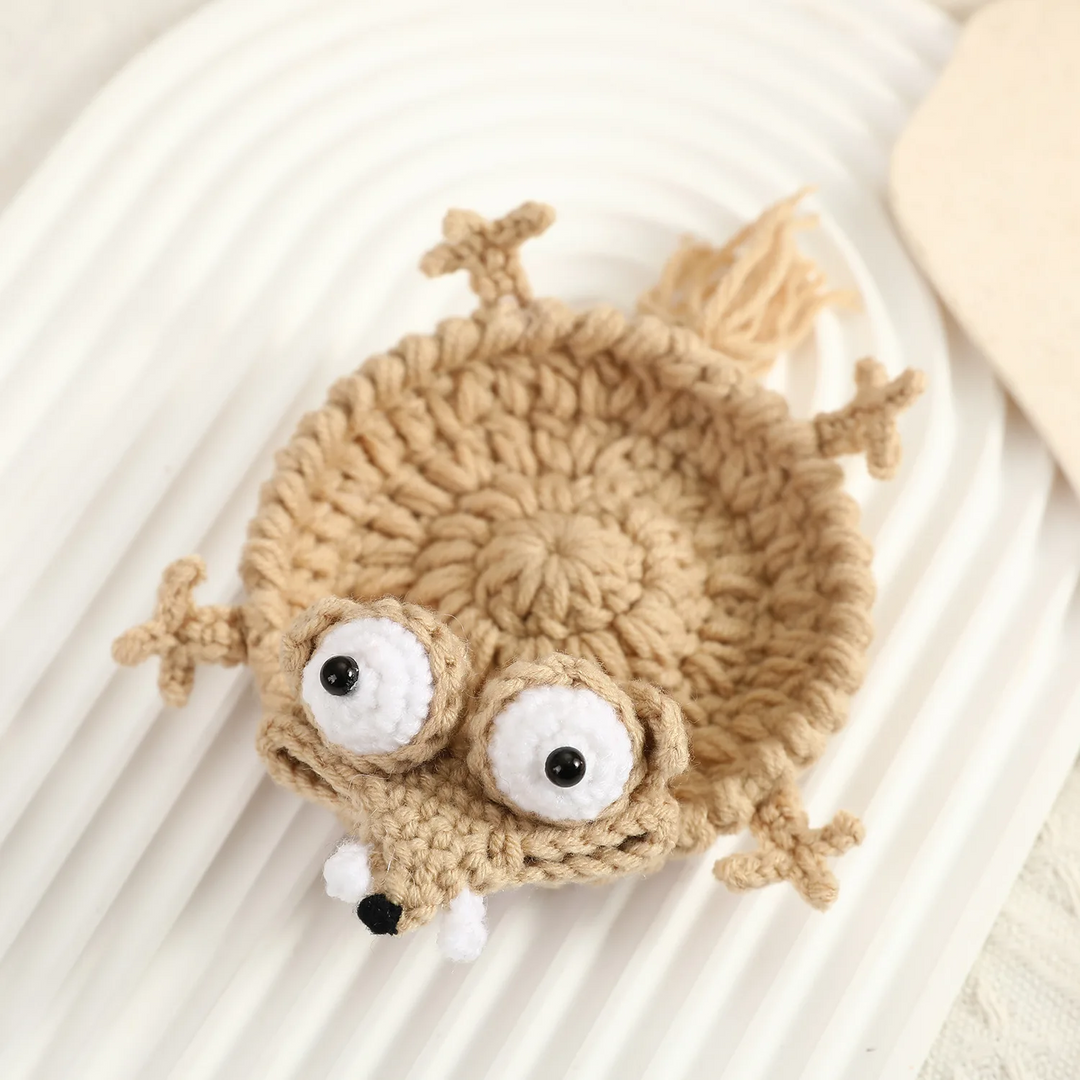 Beige crocheted animal coaster with oversized eyes, small paws, and a pointed snout