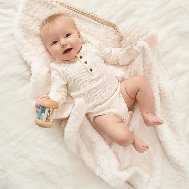 Baby lying on the white sherpa side of a beige baby blanket