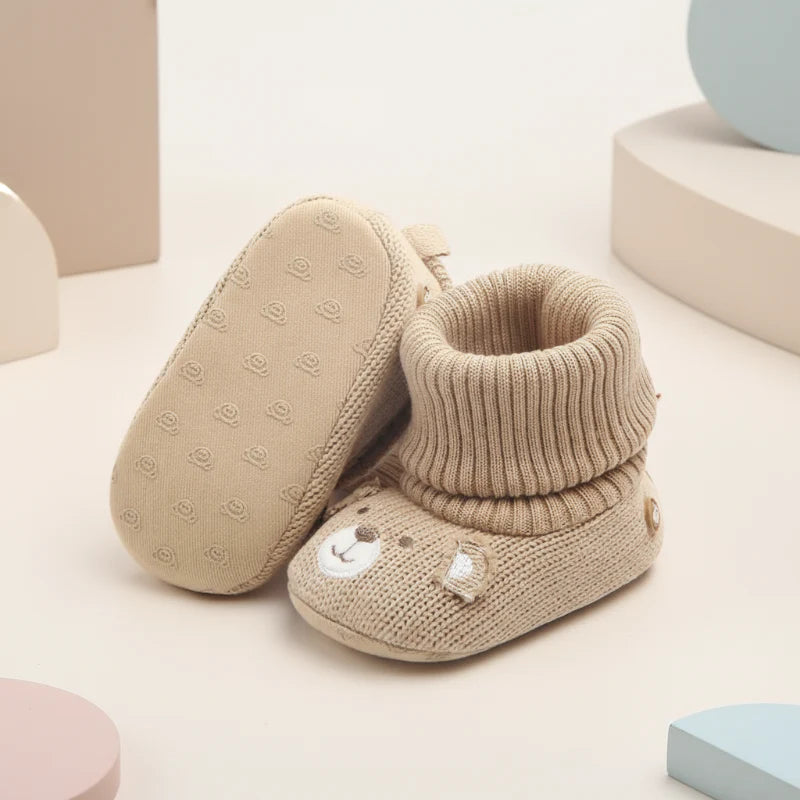 Beige baby booties showing a raised outsole pattern and a folded ribbed cuff.