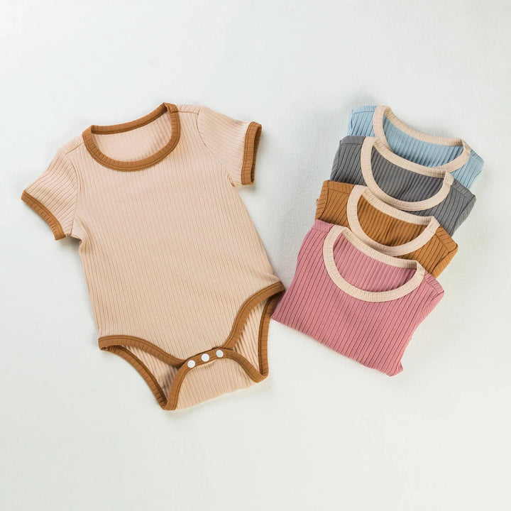 Beige ribbed baby romper with brown trim beside folded pink, blue, brown, and gray rompers