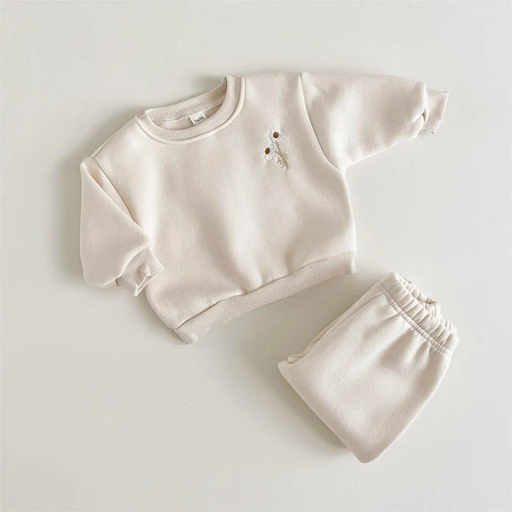 Beige floral baby sweater beside folded matching pants