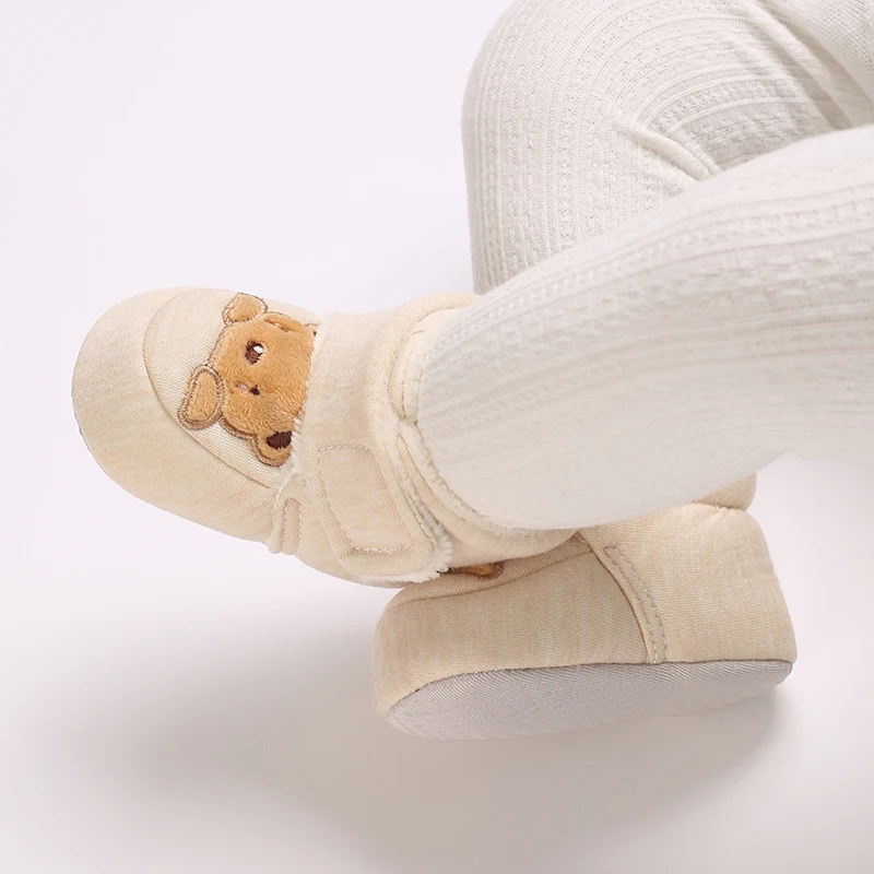 Top view of beige bear baby shoes worn with cream ribbed leggings