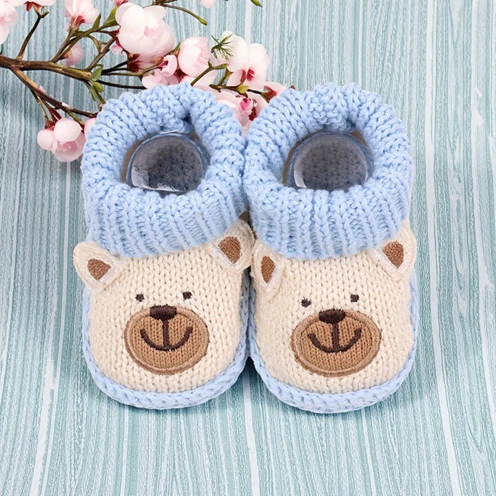Overhead view of beige bear baby booties with blue cuffs on a pale blue wooden surface
